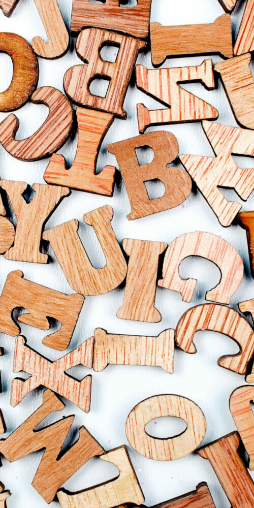 scattered mixed brown wooden letters of the English alphabet on white background, copy space, as a background composition